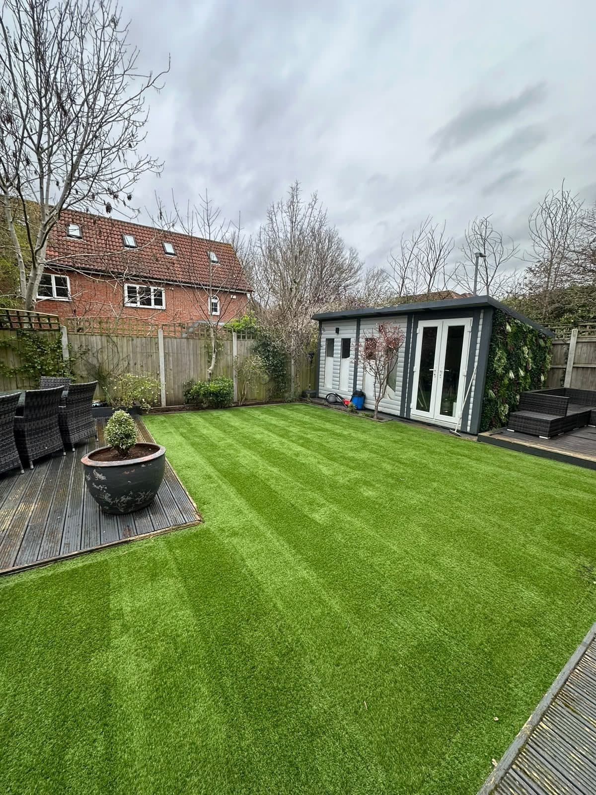 Striped artificial lawn with decking and a garden room