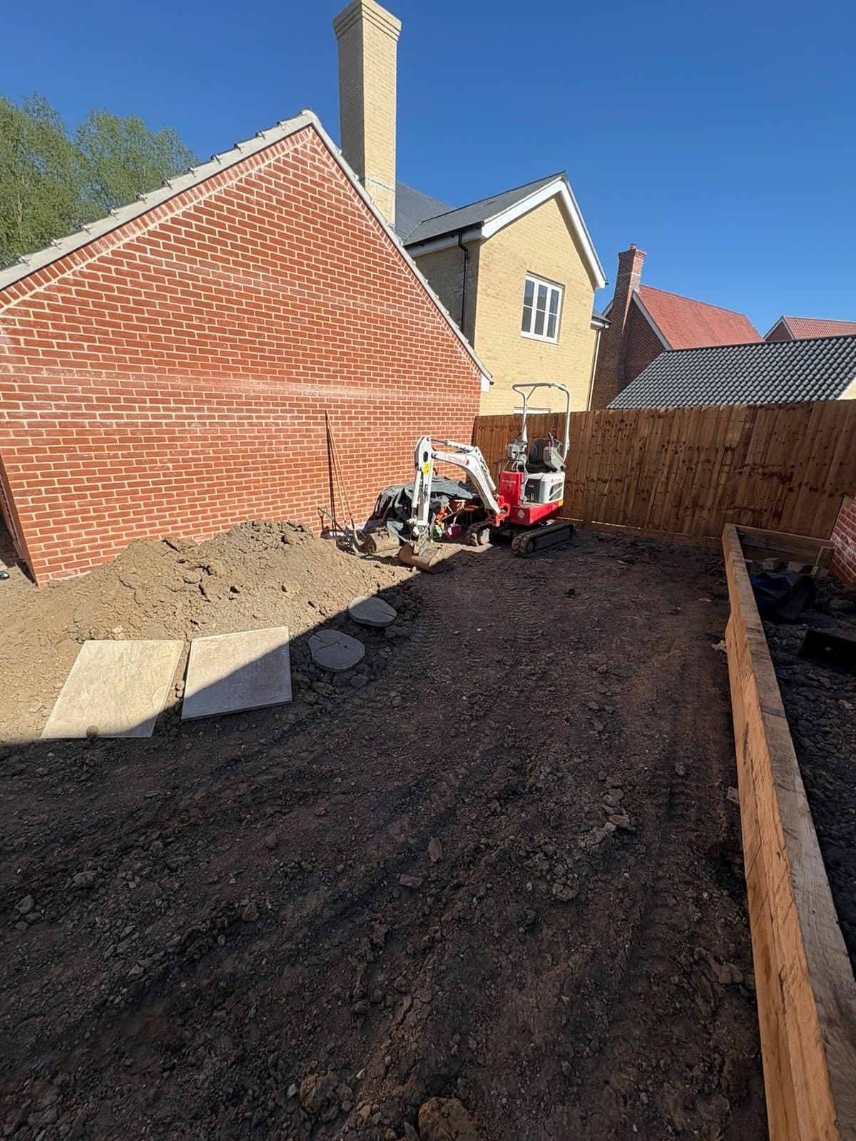 Mini digger clearing a new-build garden, with sleeper beds in place